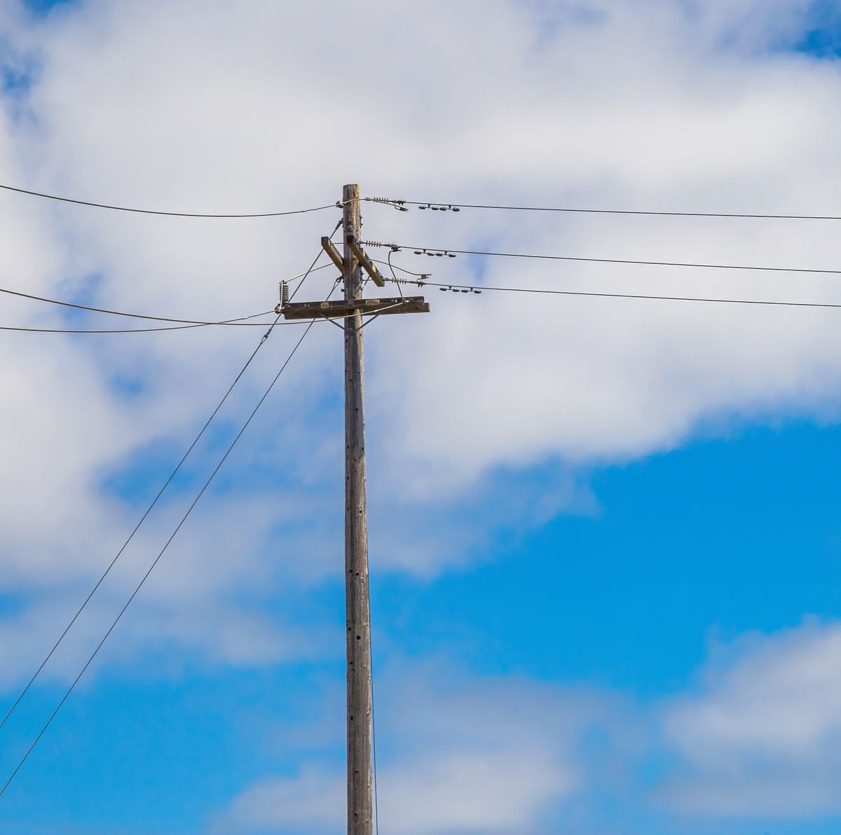 Telephone pole against a blue sky with clouds, representing the electric grid that carries power to homes