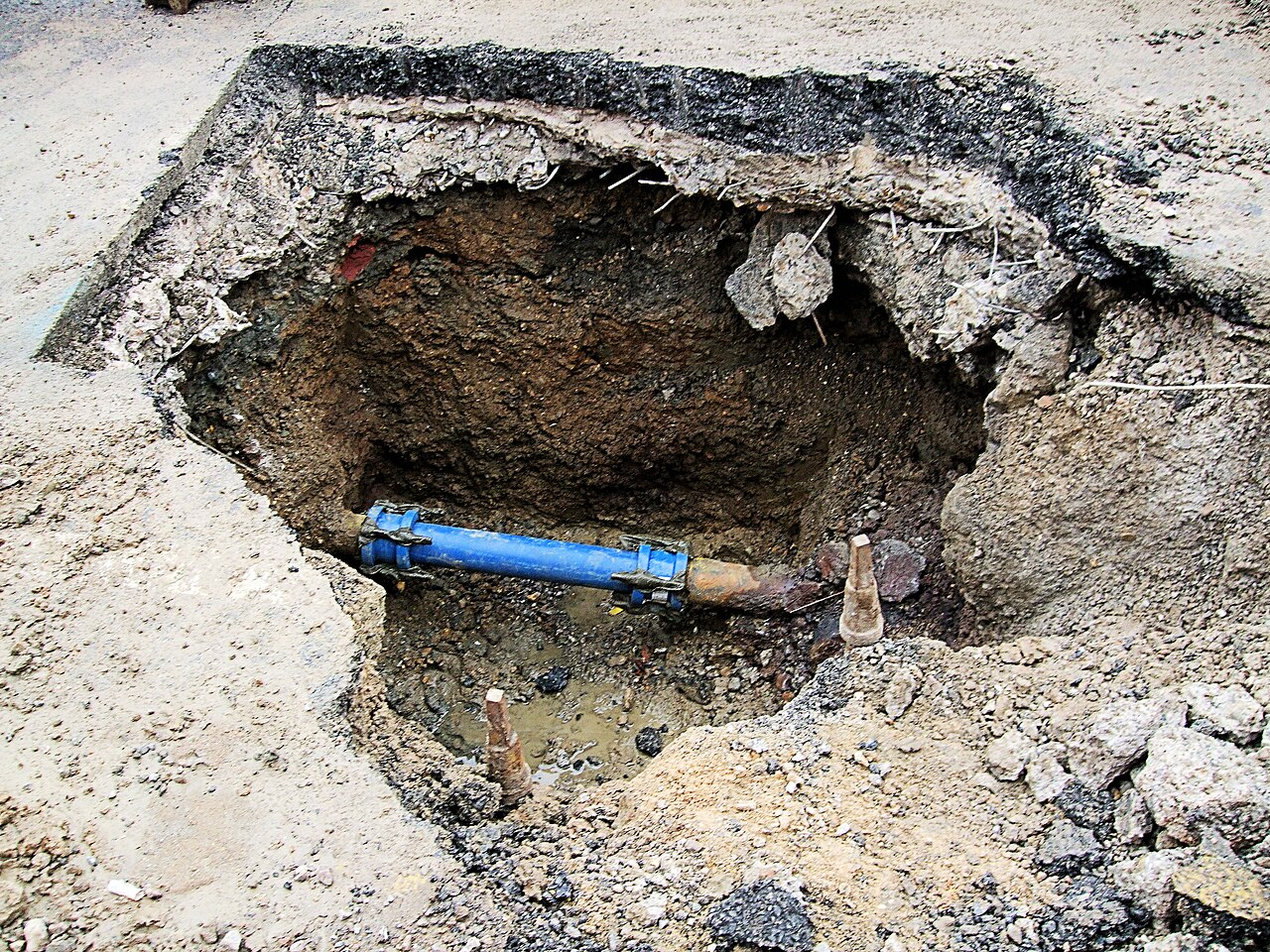 Water main under repair in a street excavation, with a blue pipe exposed in the hole